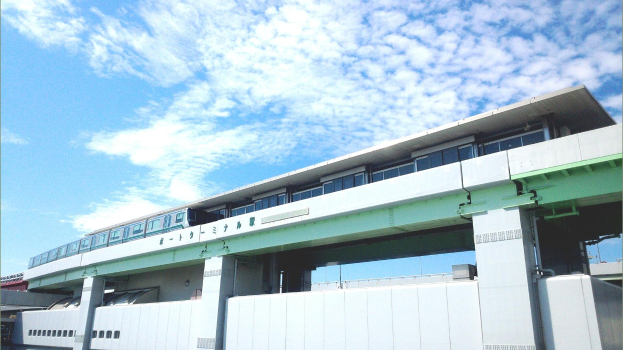 Ein Monorail-Zug, der über eine Brücke mit Säulen und Geländern fährt, umgeben von Gebäuden und einem bewölkten Himmel.