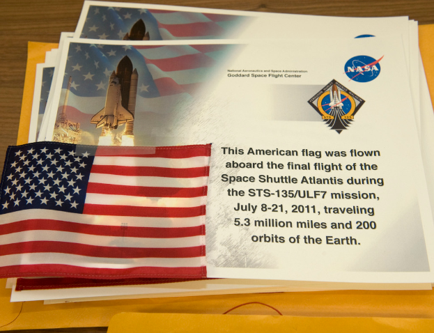 Ein zentrales Display zeigt Plakate mit Text, eine Flagge, eine Rakete und verschiedene Logos, mit einem Tisch unten und einem Boden oben im Bild.