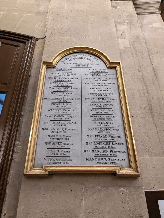 Ein gerahmtes Schild an der Seite eines Gebäudes mit einem Fenster und einer Tür, das Text enthält, wahrscheinlich ein Denkmal für die Verstorbenen.
