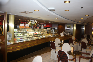 Ein Restaurant-Innenraum mit Tischen und Stühlen, einer Theke mit Blumenvaasen, Schildern mit Text, einem Ventilator und anderen Gegenständen unter einer Decke, die mit warmem Licht beleuchtet ist.