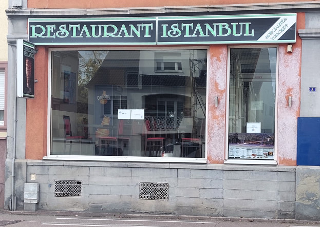 Ein Restaurant in Istanbul, Türkei, mit Glaswänden und einer Tafel mit der Aufschrift "Restaurant Istanbul", das über einer Straße hängt.