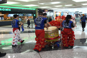 Eine Gruppe von Menschen in roter und blauer Kleidung mit Musikinstrumenten und Wagen geht durch einen hell erleuchteten Flughafen w├Ąhrend einer chinesischen Neujahrsfeier in Singapur.