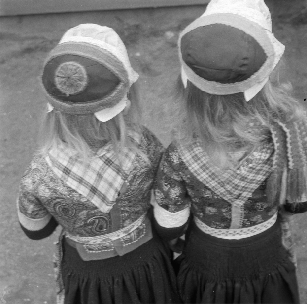 Zwei junge Mädchen in traditionellen bayrischen Trachten und Hüten stehen Seite an Seite vor einer Wand in einem Schwarz-Weiß-Foto.