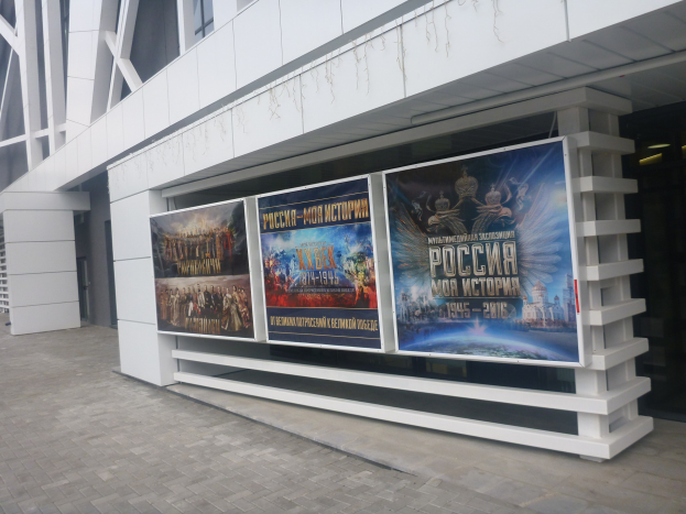 Großes Werbeplakat an einem Gebäude, das die Eröffnungszeremonie der Olympischen Spiele in Moskau ankündigt, mit beleuchtetem Gebäude auf der rechten Seite und sichtbarem Boden