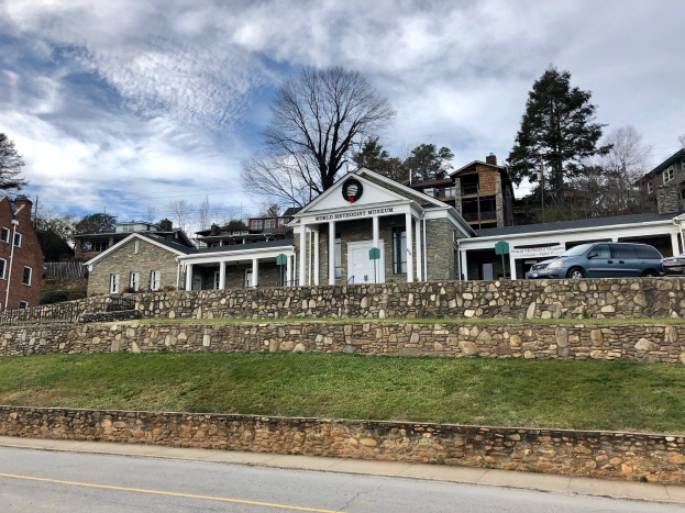 Steinwand mit geparkten Autos, angrenzende Gebäude mit Fenstern und Türen, Bäume und ein bewölkter Himmel, als das kürzlich wiedereröffnete Weltkulturerbe-Museum bezeichnet.