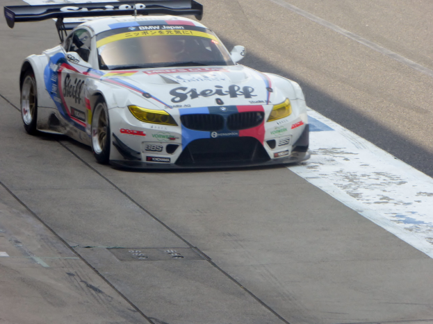 Ein strahlend blau-weißer BMW Z4 GT3 Rennauto mit großen glänzenden Rädern auf einer Rennstrecke, das eine schlankes aerodynamisches Design und ein deutliches BMW-Logo aufweist.