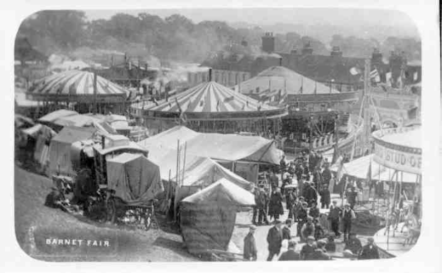 Ein altes Schwarz-Weiß-Foto einer belebten Faschings-Szene mit Zelten, Menschen, Karren, Pfählen, Bäumen und Gebäuden im Hintergrund, mit dem Text "Barnet Fair, London, England" unten.