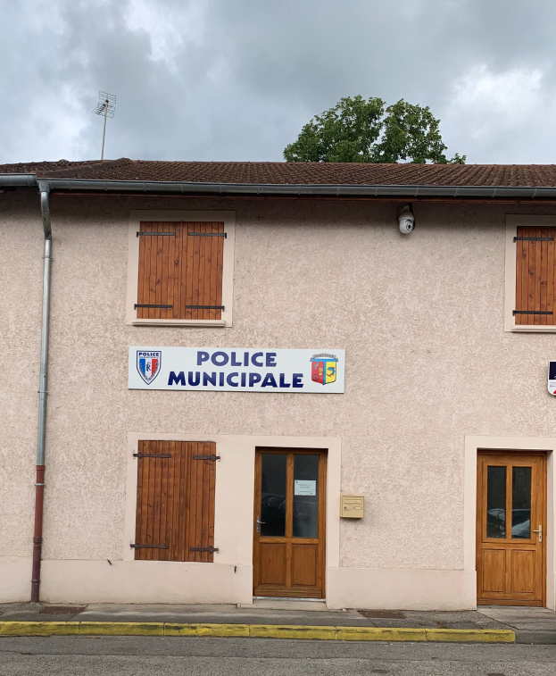 Polizeigebäude mit einem Schild, Fenstern, Türen, einer Namenskarte, einem Rohr, einem Baum und einem bewölkten Himmel im Hintergrund.