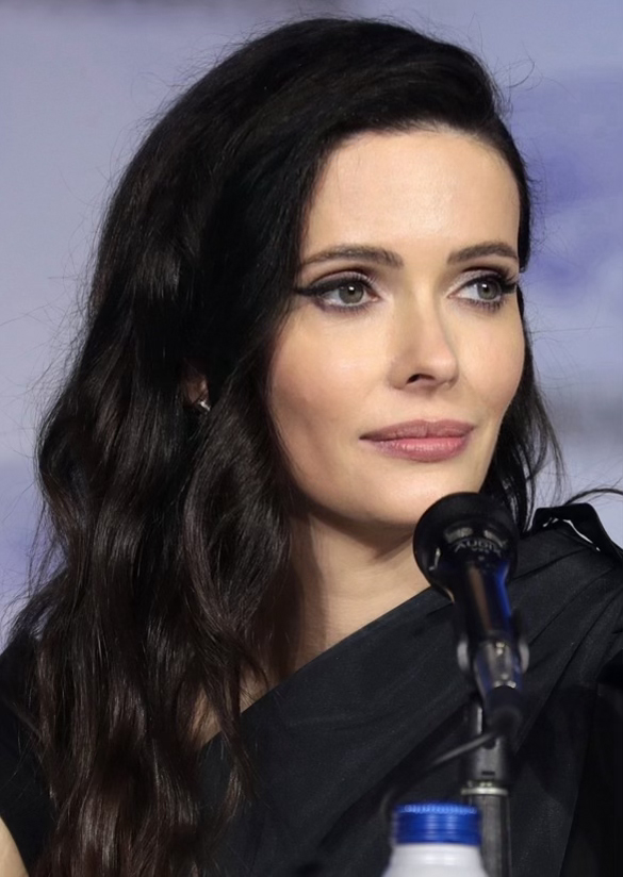 Krysten Ritter auf der Comic Con in San Diego, in einem schwarzen Kleid, vor einem Mikrofon mit einer Flasche unten, mit einem unscharfen, traumhaften Hintergrund.
