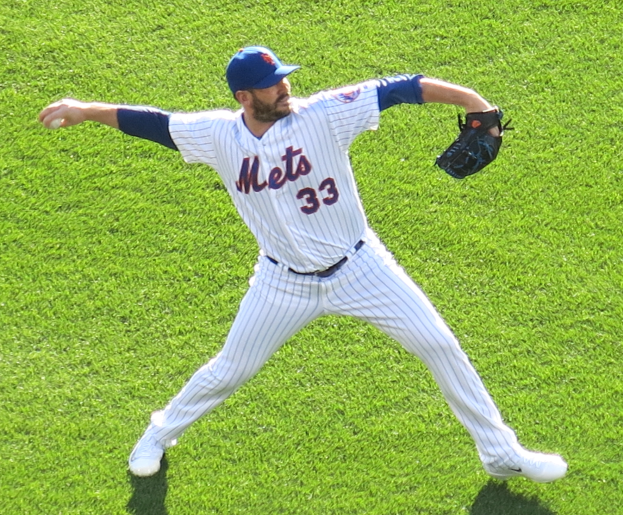 Ein Baseballspieler in einem Sportdress, einer Mütze und einem Handschuh wirft einen Ball auf einem Rasenfeld.