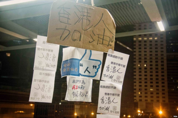 Menschen vor einem beleuchteten Gebäude bei Nacht mit Protestschildern an der Decke.