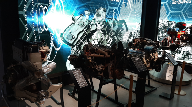 Ein Raum voller verschiedener Motoren, die auf Display-Ständern stehen und im Hintergrund Texttafeln mit Maschinen zeigen, mit einem prominenten Rad im Bild.