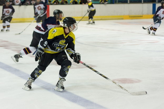 Menschen, die Schnee-Hockey mit Hockey-Schlägern und Helmen spielen, mit anderen und einer Wand im Hintergrund.