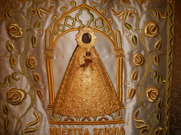 Goldbestickte Chasuble mit einer friedlichen Frau in einem hochgeschlossenen, langärmeligen Kleid mit einem Dutt, umgeben von detaillierten Texten und prächtigen goldenen Designs.