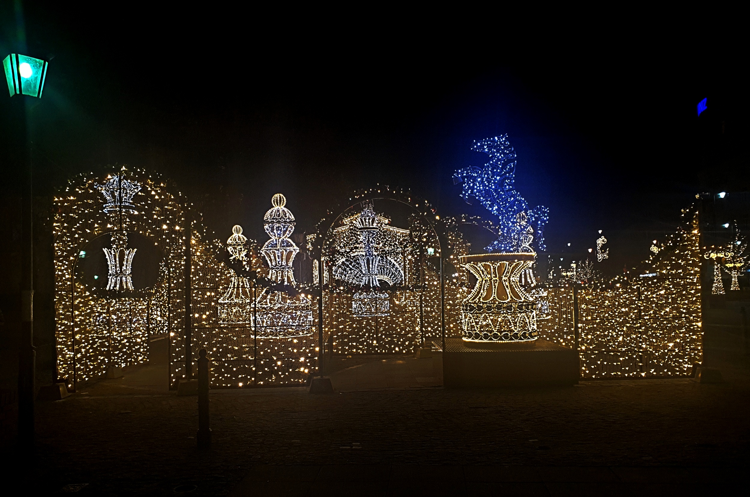 Eine nächtliche Parkszene mit Weihnachtslichtern in dekorativer Anordnung, beleuchtet von einer Straßenlaterne links daneben.