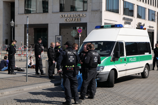 Gruppe von Polizeibeamten vor einem Starbucks-Café mit einem Van auf der rechten Seite und Menschen auf der linken Seite, Hintergrund enthält ein Gebäude mit Fenstern, ein Schild, einen Laternenpfahl und eine Absperrung.