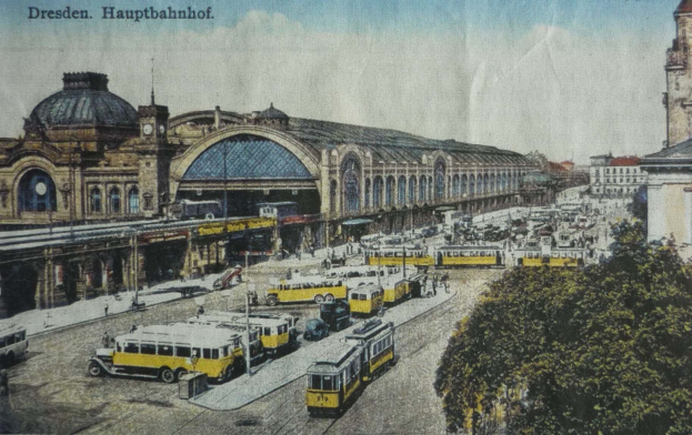Schwarz-weiß-Postkarte des Dresdner Hauptbahnhofes in Deutschland, die eine belebte Straßen Szene mit Fahrzeugen, Fußgängern, Bäumen, Gebäuden und einem bewölkten Himmel zeigt.