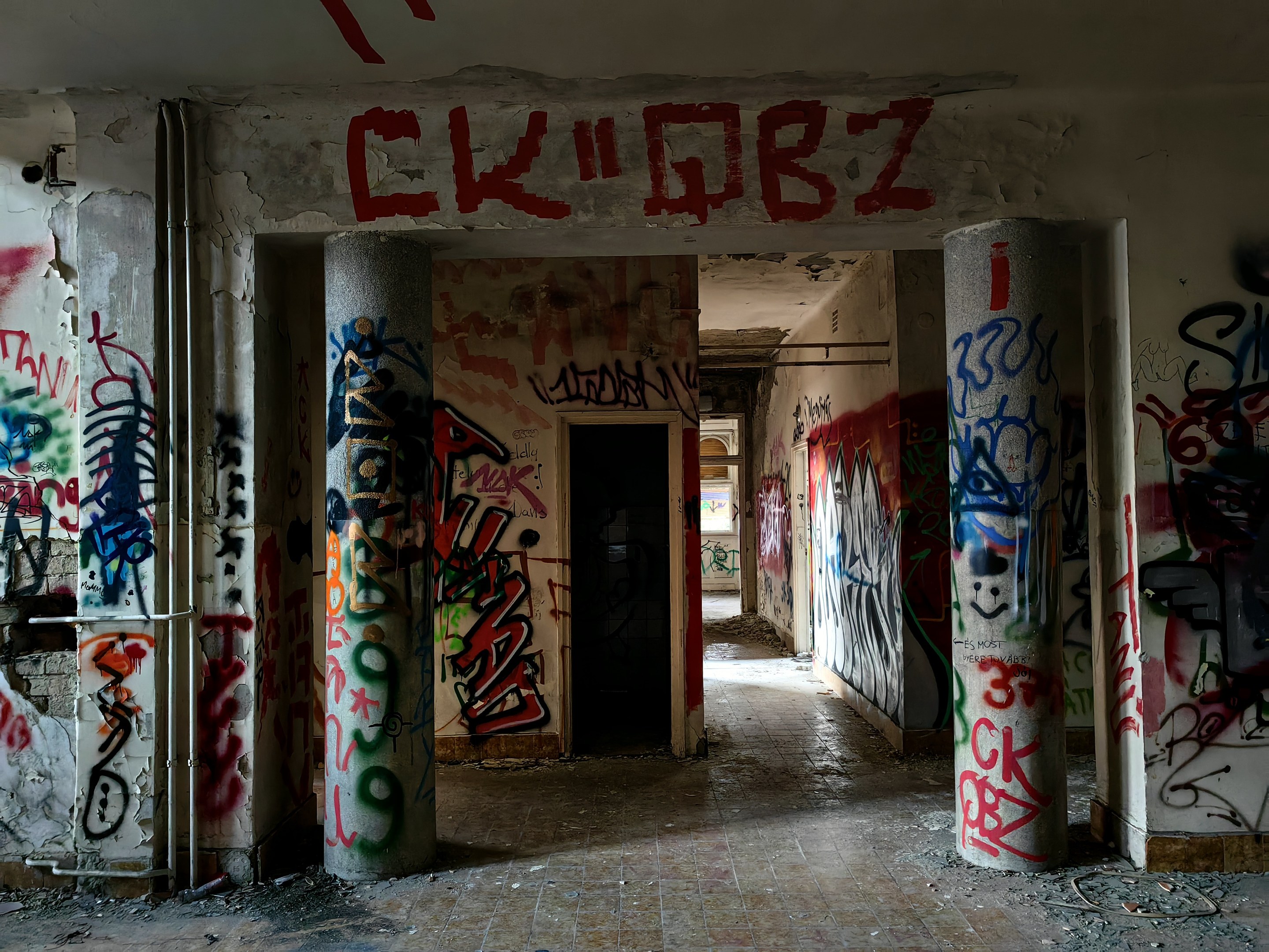 Verlassenes Gebäude mit graffiti-bedeckten Wänden, sichtbarem Boden, freiliegenden Rohren und einer Tür im Hintergrund, das die städtische Verwahrlosung zeigt.