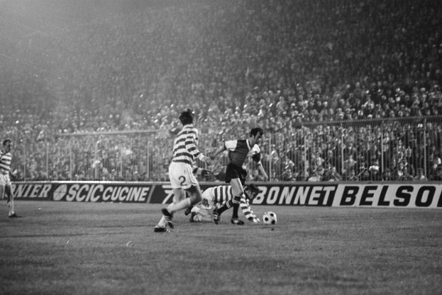 Ein Schwarz-Weiß-Bild von Männern, die auf einem Feld Fußball spielen, mit Zuschauern auf den Tribünen und einer Tafel mit der Aufschrift "Celtic v West Bromwich Albion - FA Cup Third Round."