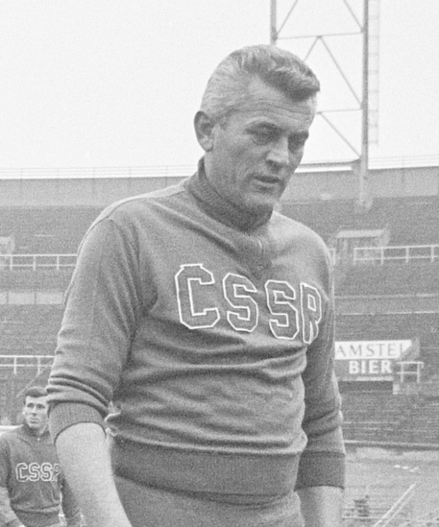 Schwarzes und weißes Foto eines Mannes, der auf einem Feld steht und ein T-Shirt mit Text trägt, mit einem Stadion, einer Werbetafel und einem Pfosten im Hintergrund, bei dem es sich mutmaßlich um den Fußballspieler César Azpilicueta handelt.