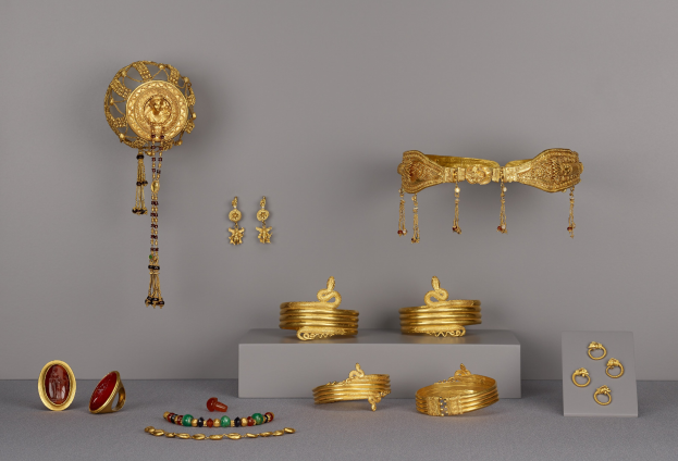 Goldschmuck-Display mit Armbändern, Ringen und anderen Stücken auf einer Oberfläche, mit zusätzlichen Teilen an der Wand im Hintergrund.