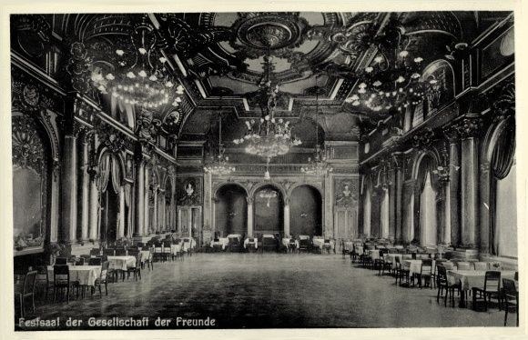 Schwarz-weiß-Foto eines großen Raums mit Tischen, Stühlen, Säulen, Bögen und Kronleuchtern, beschriftet mit 'Festival der Gesellschaft der Freunde, Berlin' unten.